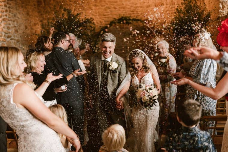 Wedding photograph by Sky Photography — a couple walk back down the aisle through confetti thrown by their guests